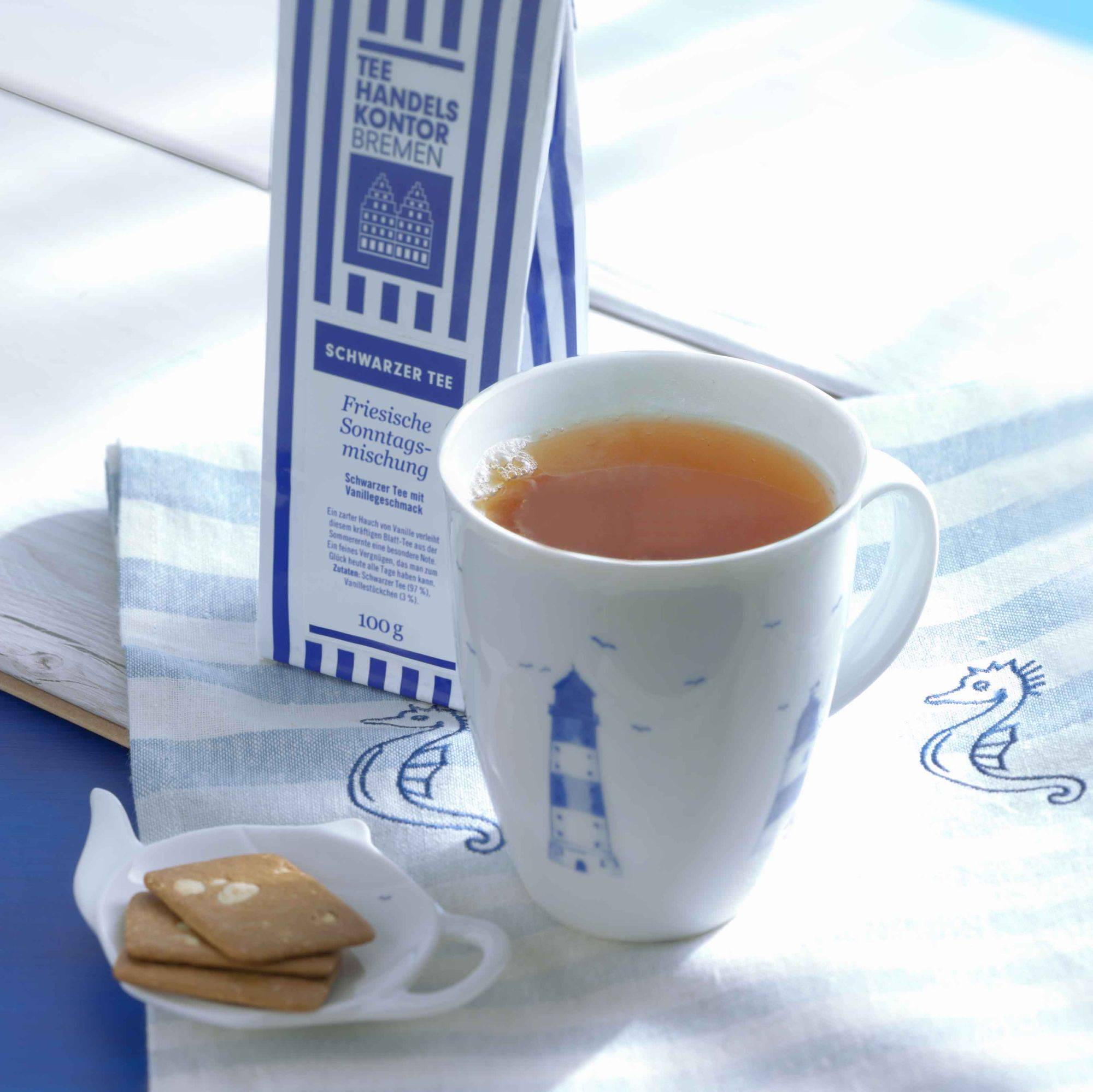 Dekoratives Bild: maritimer weißer Porzellanteemug mit blau-weißer Teetüte und Gebäck