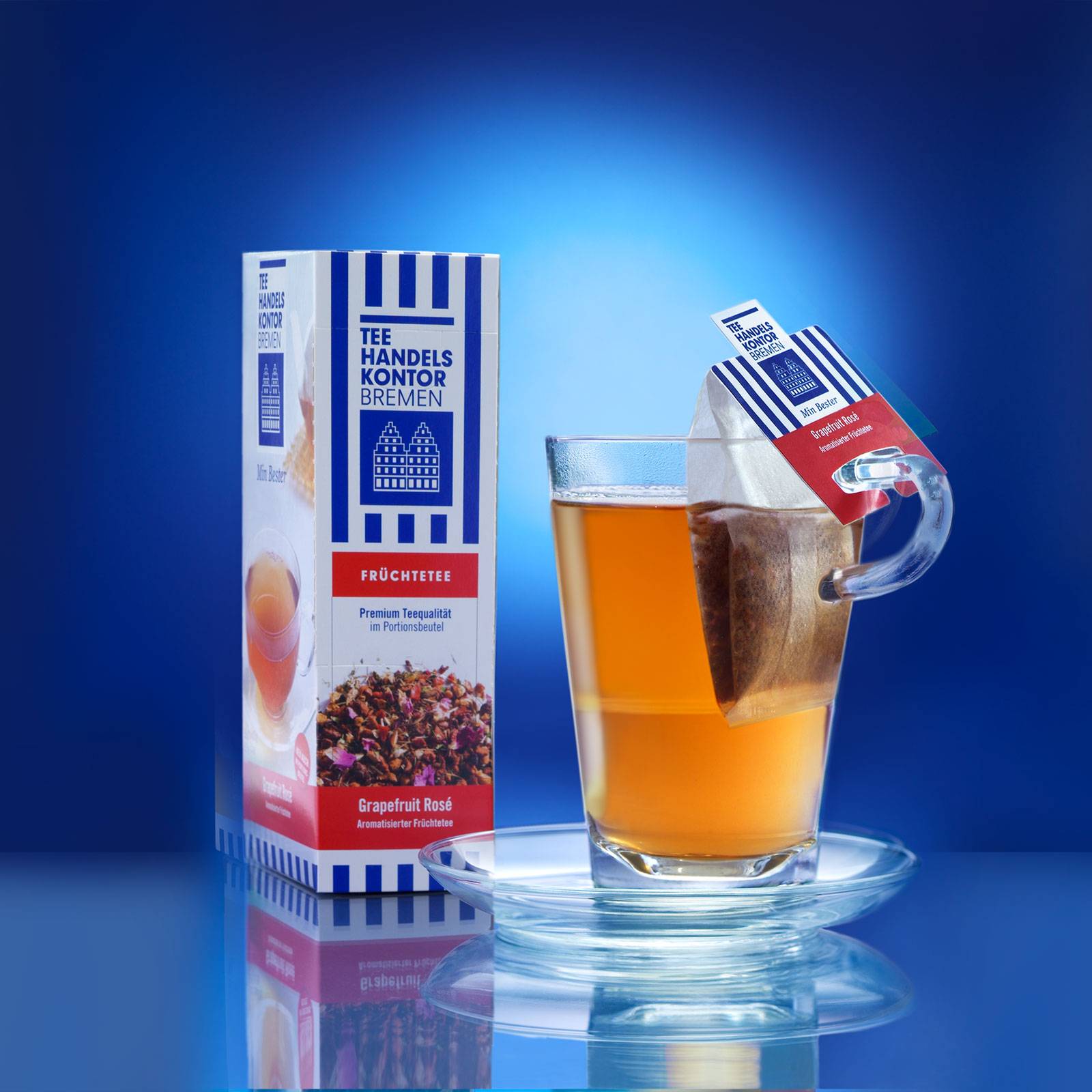 Dekobild: Teepackung vor blauem Hintergrund und Teeglas mit aufgebrühtem Tee und Teebeutel