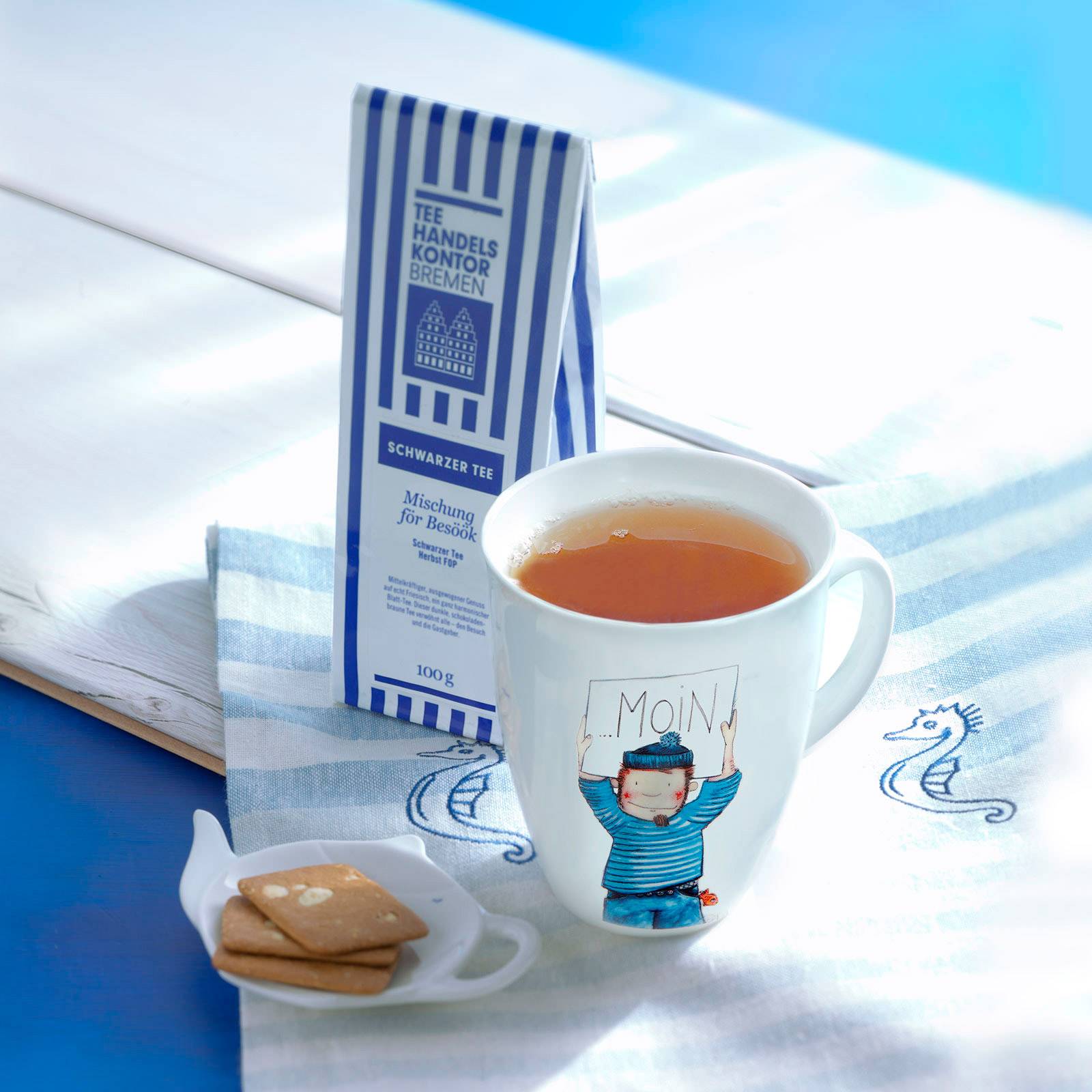 Dekoratives Bild mit aufgebrühtem Schwarztee in Porzellanbecher und blau-weiß gestreifte Teetüte