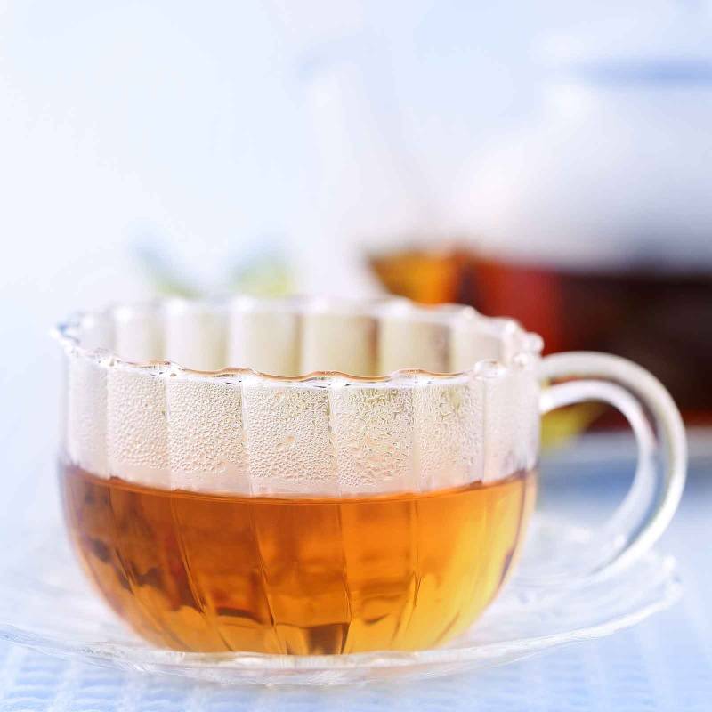 Dekobild: Tee in einer geriffelten Glasteetasse mit Kanne in der Unschärfe
